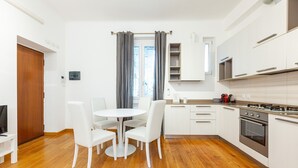 Eine moderne Küche mit weißen Schränken, einem eingebauten Backofen und einem Essbereich mit rundem Tisch und weißen Stühlen.