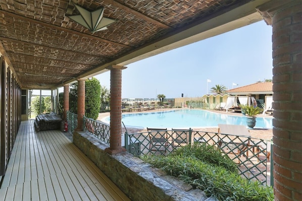 A covered outdoor area with a pool, wooden deck, and brick columns.