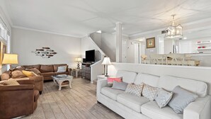 Ein Wohnzimmer mit braunem Sofa, weißem Sofa, Couchtisch und Fernseher. Eine Treppe führt in einen anderen Raum.
