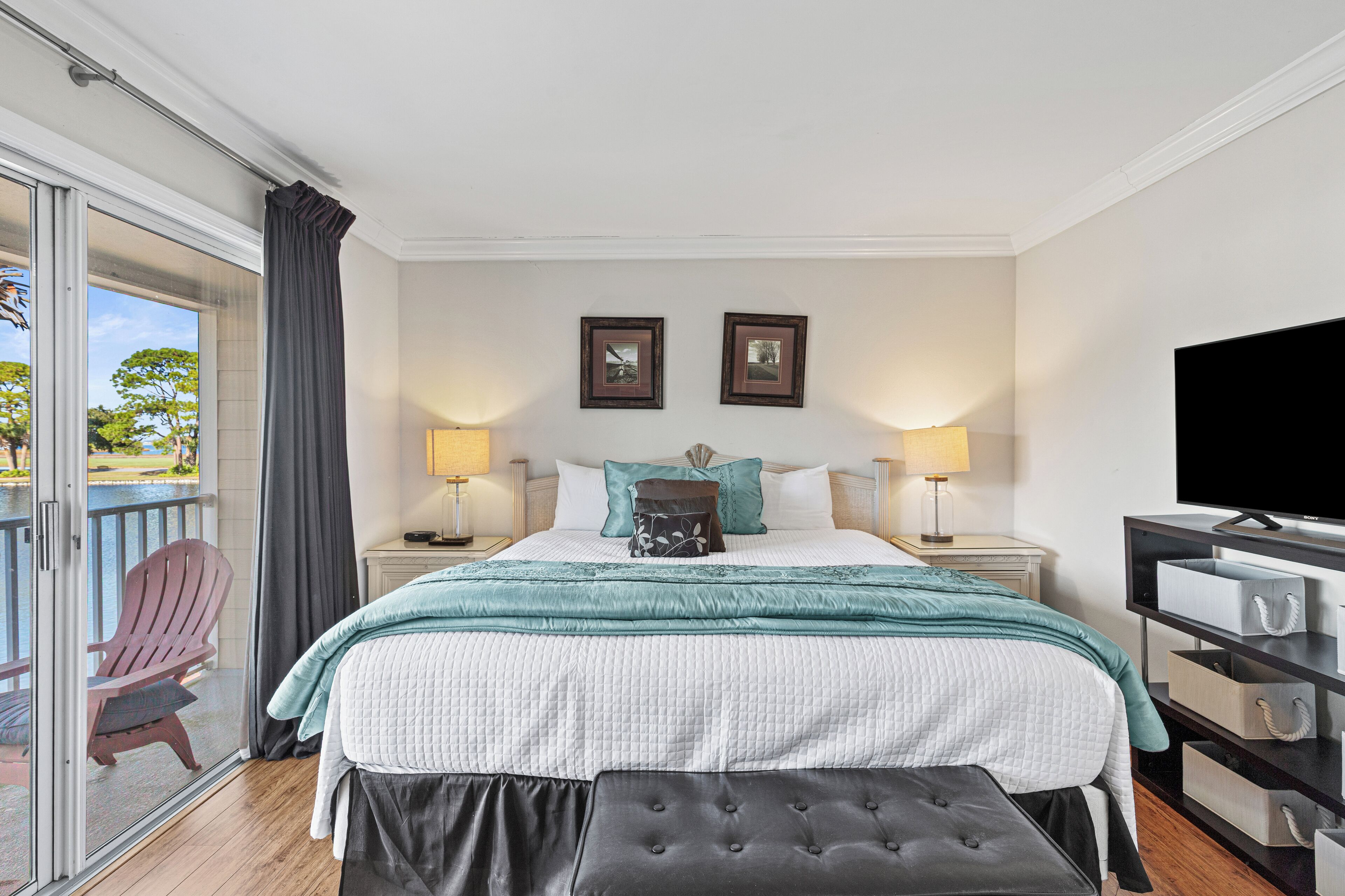 A bedroom with a bed, two bedside tables with lamps, a TV, a sliding glass door, and a chair.