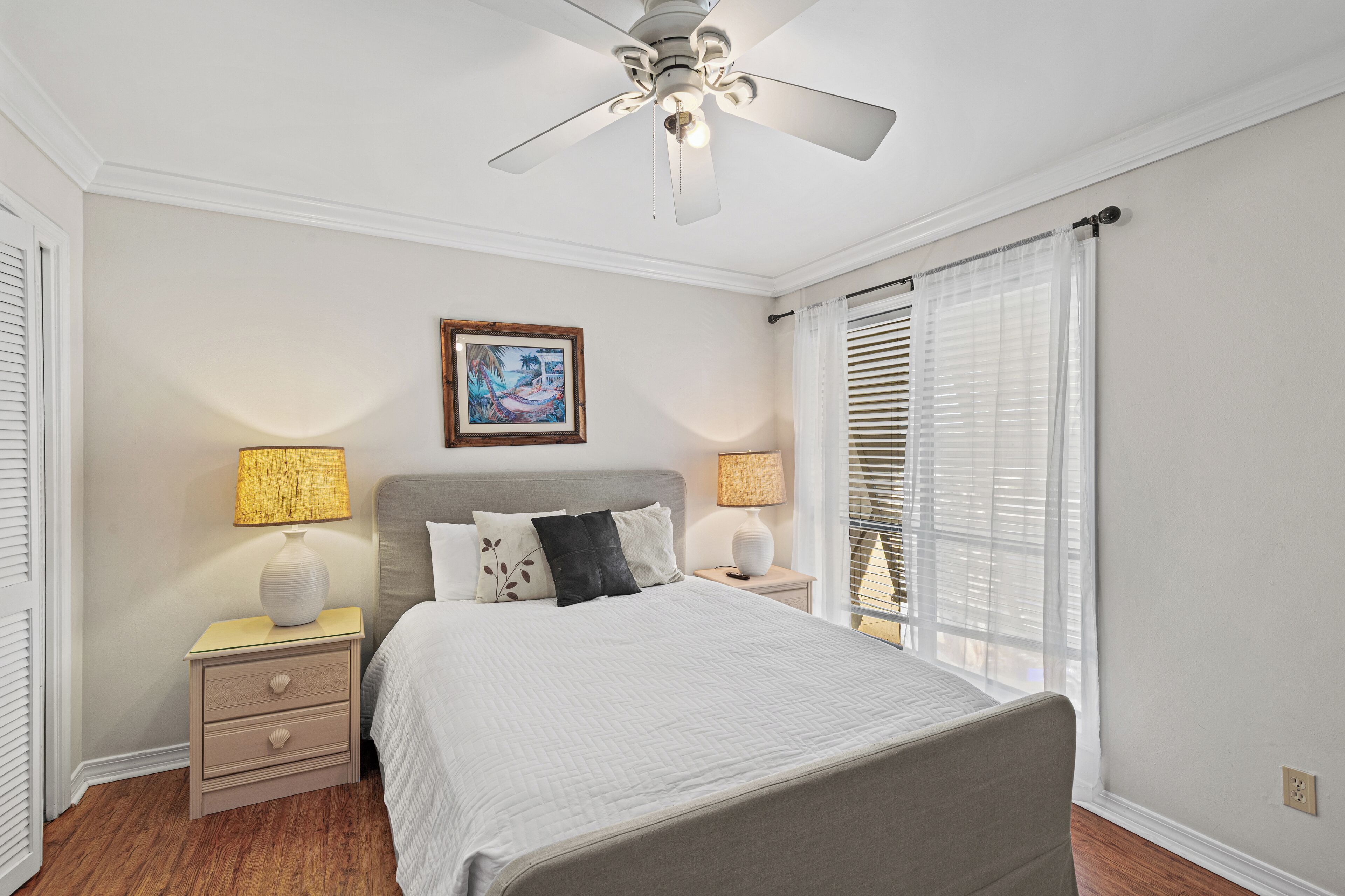 A bedroom with a bed, two bedside tables, a ceiling fan, and a window with blinds.