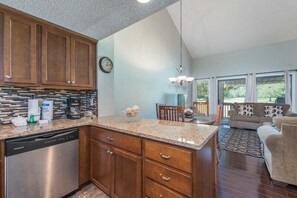 A kitchen with wooden cabinets, a dishwasher, and a dining area with a sofa and table.