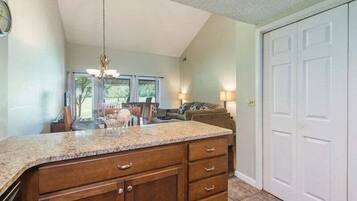 A kitchen with a granite countertop, wooden cabinets, a hanging light fixture, and a view of the dining area.