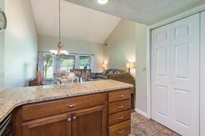 A kitchen with a granite countertop, wooden cabinets, a hanging light fixture, and a view of the dining area.