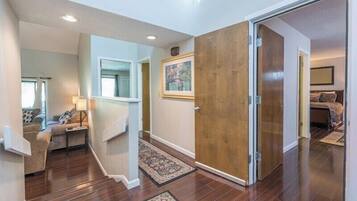A hallway with a wooden door, a rug, a framed picture, and a bed in the background.