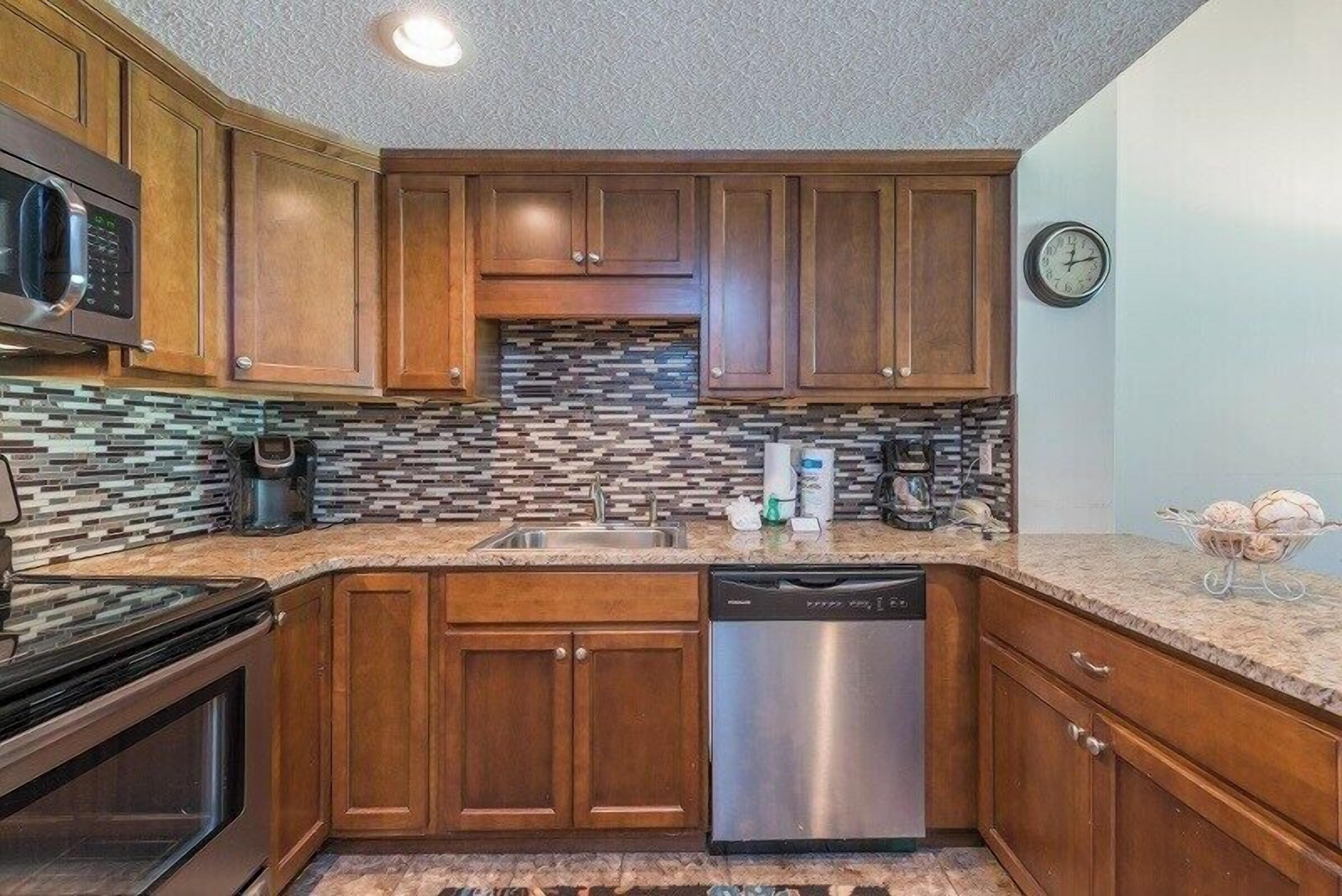 Cozinha compacta com armários de madeira, lava-louças, micro-ondas e painel de azulejos.
