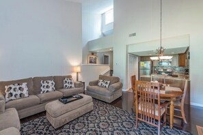 A living room with a sofa, ottoman, and a dining table with chairs. There is a patterned rug on the floor.