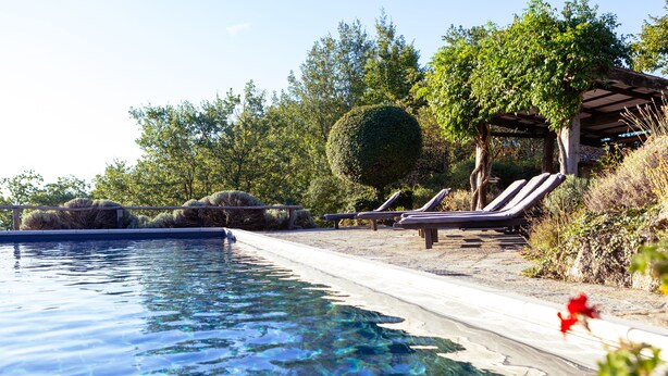 En swimmingpool med krystalklart vand, liggestole og et pergolaoverdækket område.