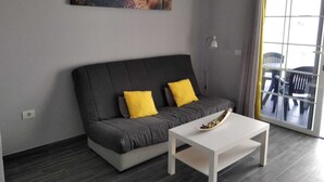 En moderne stue med en grå sofa, to gule puder, et hvidt sofabord og et maleri af en strandscene på væggen.