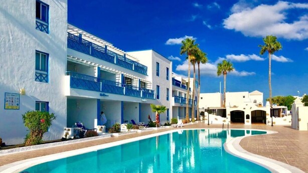 Et hotel med swimmingpool, flere balkoner og palmer.