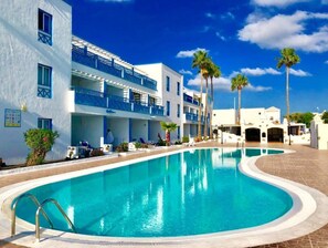Ein Hotel mit Swimmingpool, mehreren Balkonen und Palmen.