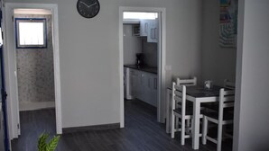Et moderne køkken med hvide skabe, en mikrobølgeovn og en kaffemaskine. Der er et spiseområde med et bord og stole.