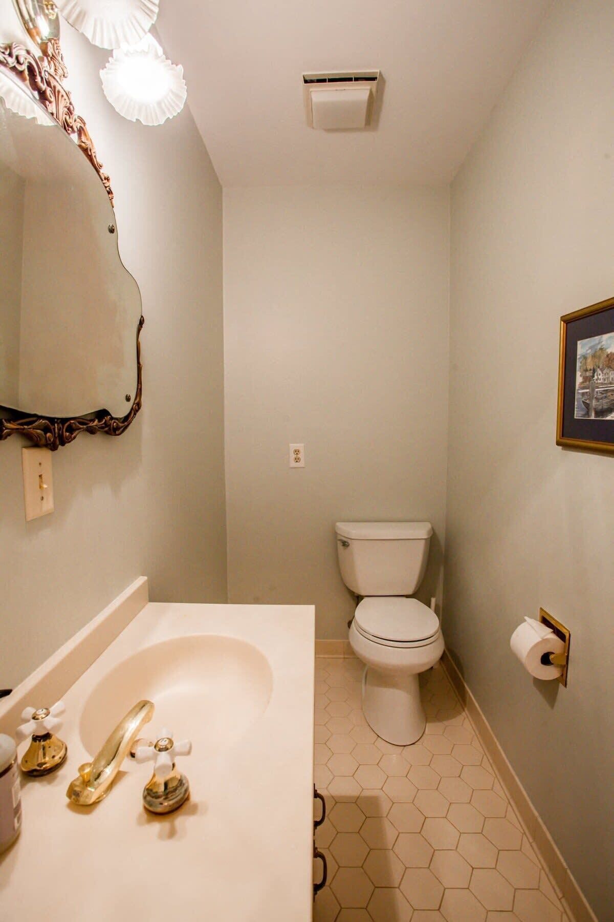 Un baño con un lavabo blanco, grifos dorados, un inodoro y un espejo con un marco decorativo.