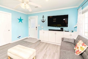 A room with a television, a sofa, a ceiling fan, and a star decoration on the wall.