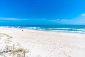 A beach with a clear sky, sandy shore, and a person sitting on the sand.