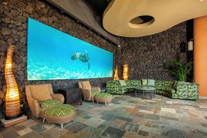 Eine Lobby mit großem Wandbild, Steinwänden und einer Sitzecke mit Korbmöbeln.