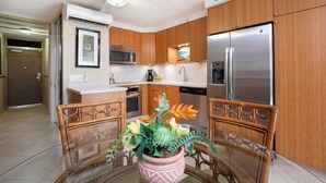 Une cuisine moderne avec des meubles en bois, des appareils électroménagers en acier inoxydable, une table à manger en verre et un ventilateur de plafond.