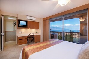 A hotel room with a bed, a desk, a television, and a balcony with a view of the sea.