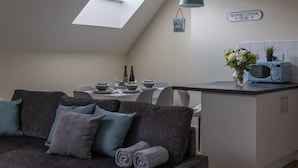 Une cuisine moderne avec un coin repas, un canapé gris avec des coussins, une lucarne, un four à micro-ondes et un panneau décoratif au mur.