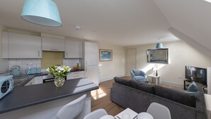 Une cuisine moderne avec des meubles blancs, un plan de travail gris et un luminaire suspendu bleu.
