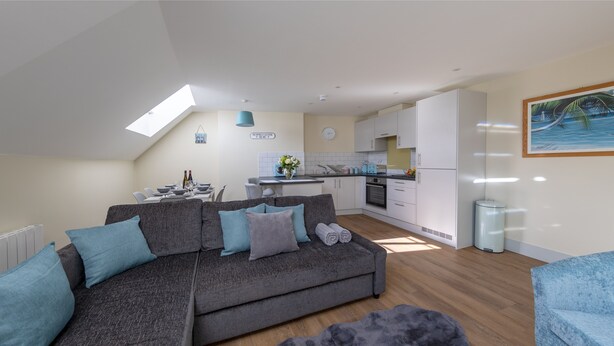 Un appartement moderne avec un canapé gris, un fauteuil bleu, un coin repas et une cuisine.