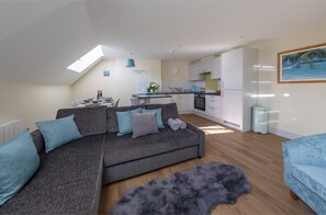 A modern apartment with a grey sofa, a blue armchair, a dining area, and a kitchen. - Apartment 8 Isabella House Hereford (Hereford)
