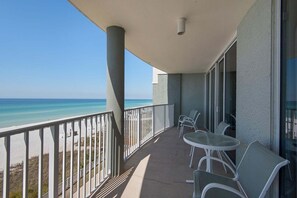 A balcony with a view of the beach and ocean, featuring a table and chairs. - Oceanfront bliss awaits in this cozy 1-bedroom condo at Panama City Beach. (Panama City Beach)