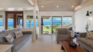 A spacious living room with a large sofa and armchairs, a coffee table, and a view of the ocean through large sliding glass doors.