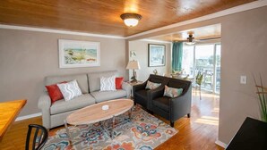 A living room with a sofa, a coffee table, and a patterned rug. There are two side tables with lamps. The room has wooden flooring and a ceiling with a light fixture. - Wanna Sea #201 - Newly Constructed Balcony! (Fernandina Beach)