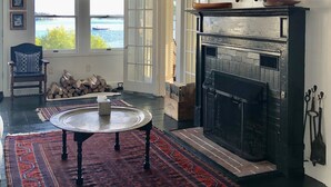 Un salon spacieux avec une grande cheminée, une table ronde et un tapis rouge à motifs.