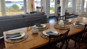 Un coin repas avec vue sur l’eau, une table en bois dressée avec des assiettes et des serviettes, et un canapé en arrière-plan.
