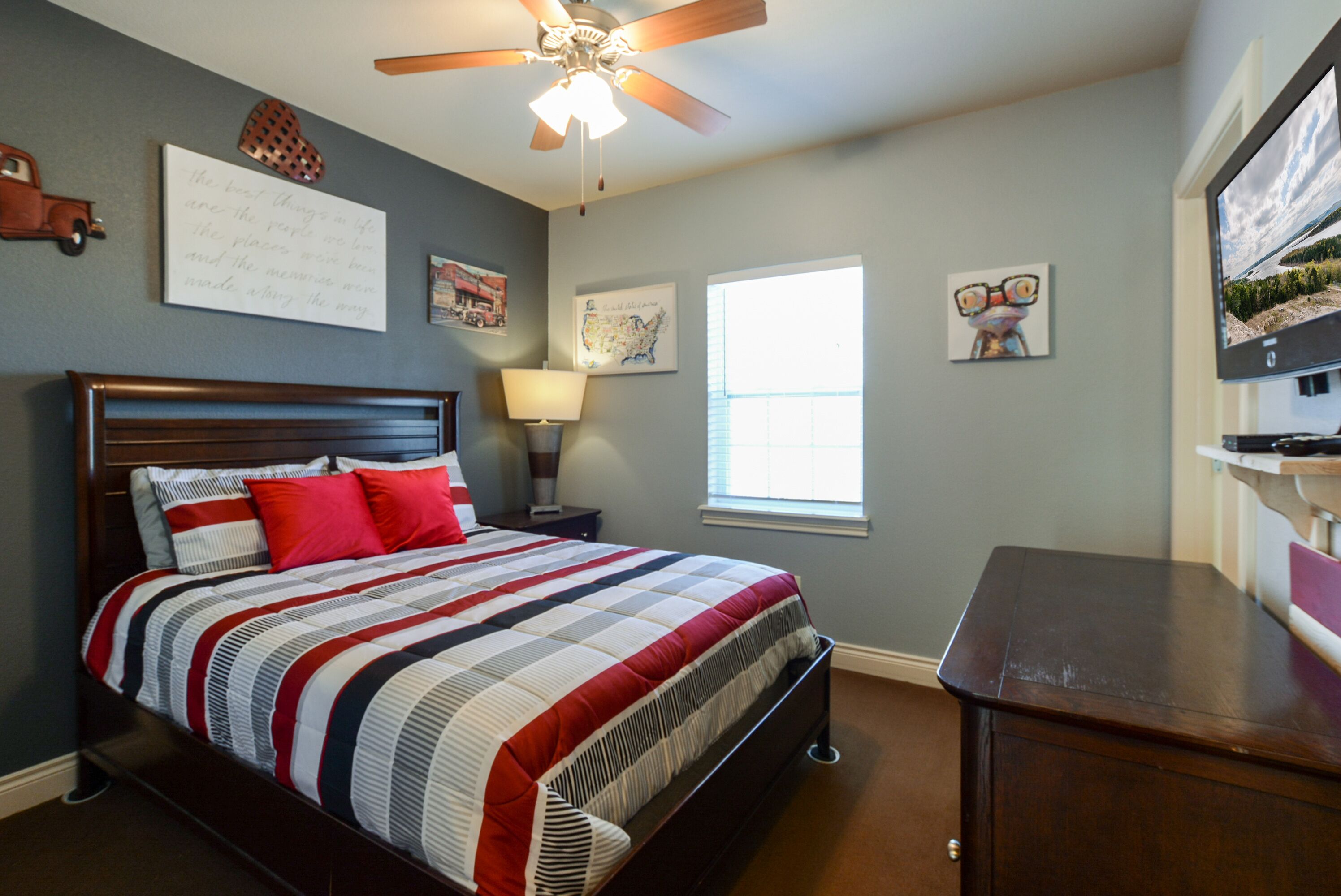 A bedroom with a bed, a ceiling fan, a window, and a desk.