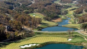A golf course with multiple ponds, surrounded by wooded areas and a few buildings.