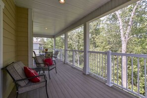 Relax on the covered porch with comfortable seating and a small table, surrounded by lush greenery.
