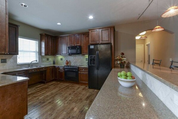 Una cocina moderna con armarios de madera, encimeras de granito, un refrigerador negro y un cuenco de fruta en la encimera.