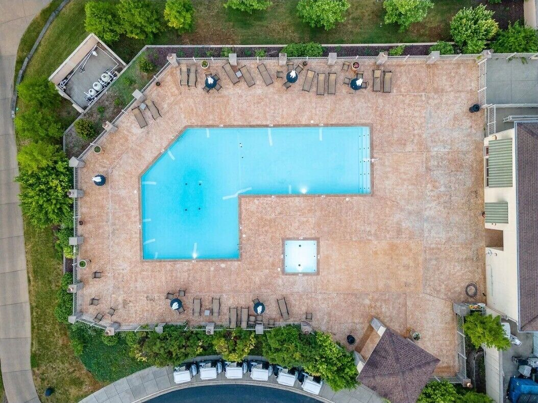 An aerial view of a swimming pool area with a rectangular pool, surrounded by lounge chairs and a small deck area.