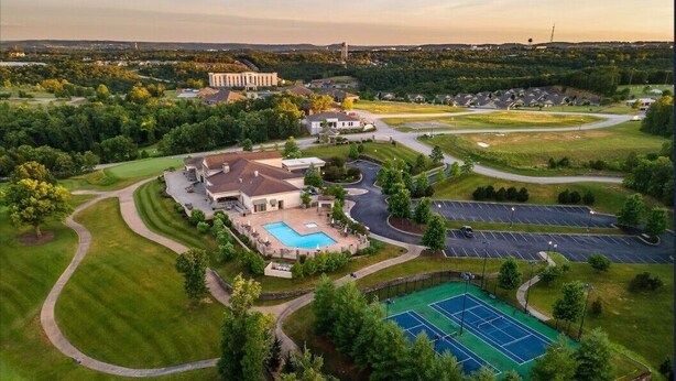 An aerial view of a golf course with a swimming pool, tennis courts, and a large building in the background.