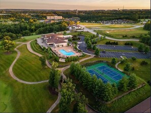 Vista aérea de un campo de golf con piscina, canchas de tenis y un edificio grande al fondo.