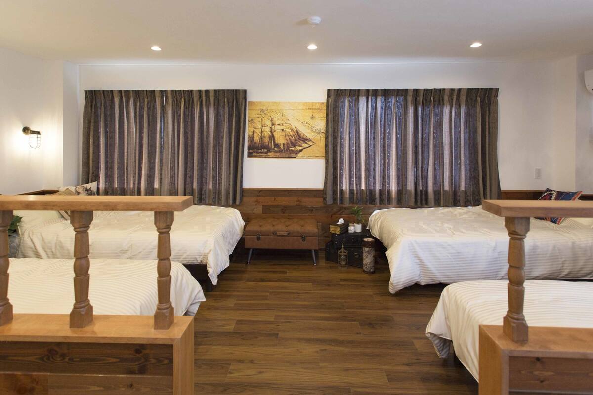 A hotel room with two beds, wooden headboards, a wooden floor, a painting on the wall, and curtains.