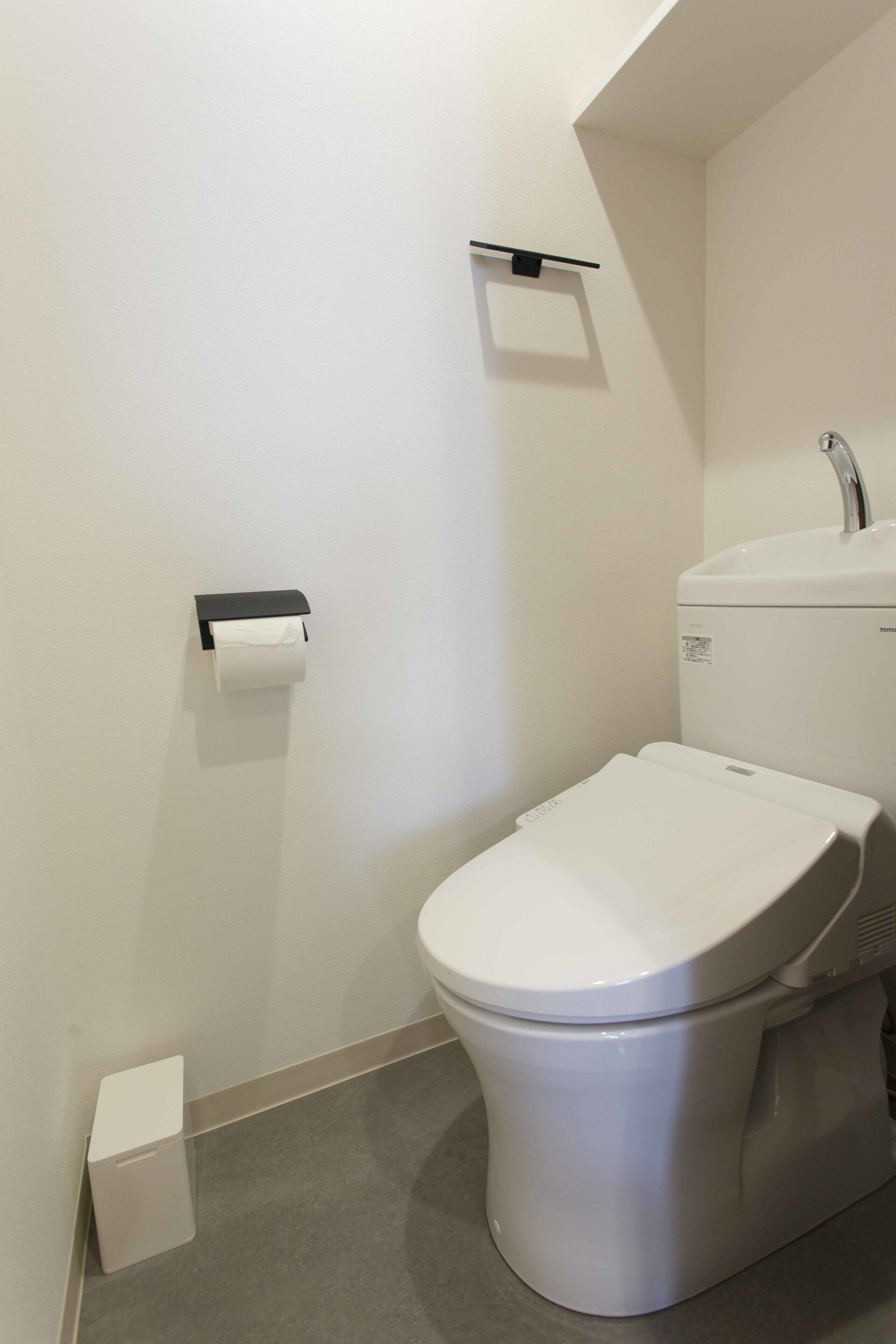 A modern bathroom with a toilet, sink, and toilet paper holder.