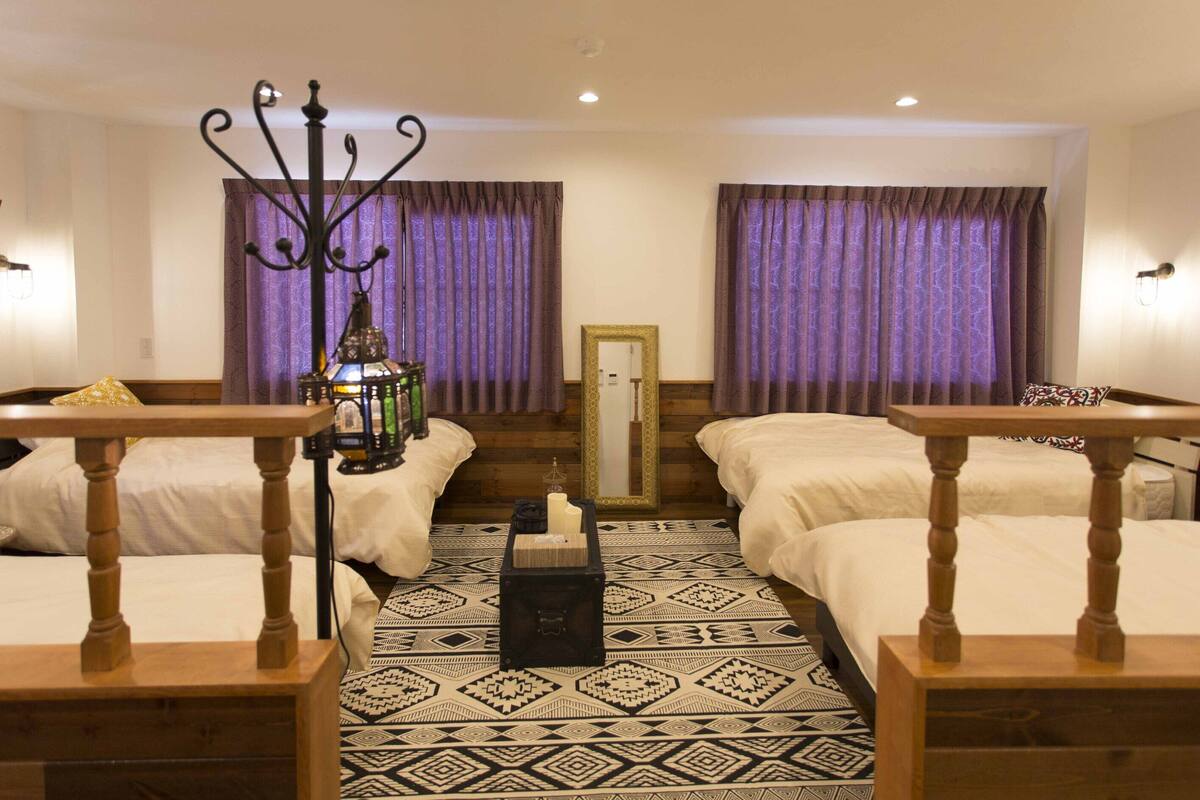 A hotel room with two beds, a wooden table, a decorative lamp, and a patterned rug.