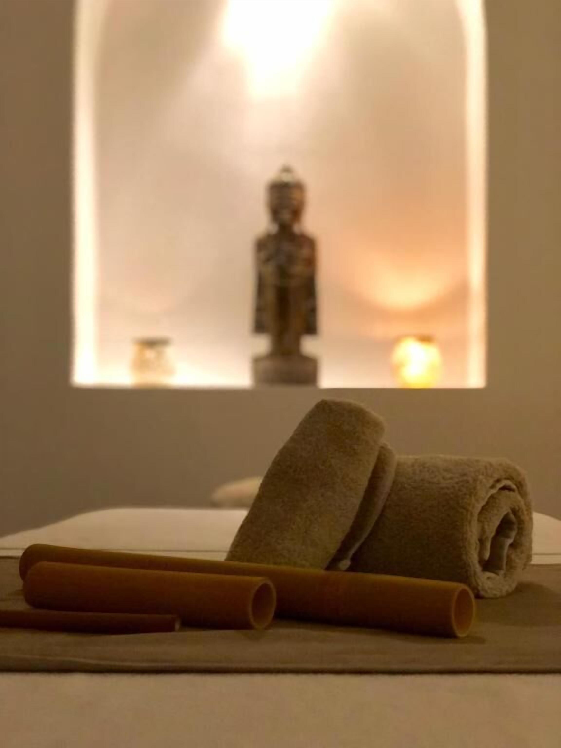A room with a meditation area featuring a statue, a candle, and rolled towels on a flat surface.