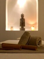 A room with a meditation area featuring a statue, a candle, and rolled towels on a flat surface.