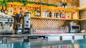 Una zona de bar con pared de madera en espiga, estantes con botellas de licor, una máquina de café y un soporte para cristalería.