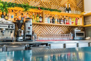 Una zona de bar con pared de madera en espiga, estantes con botellas de licor, una máquina de café y un soporte para cristalería.