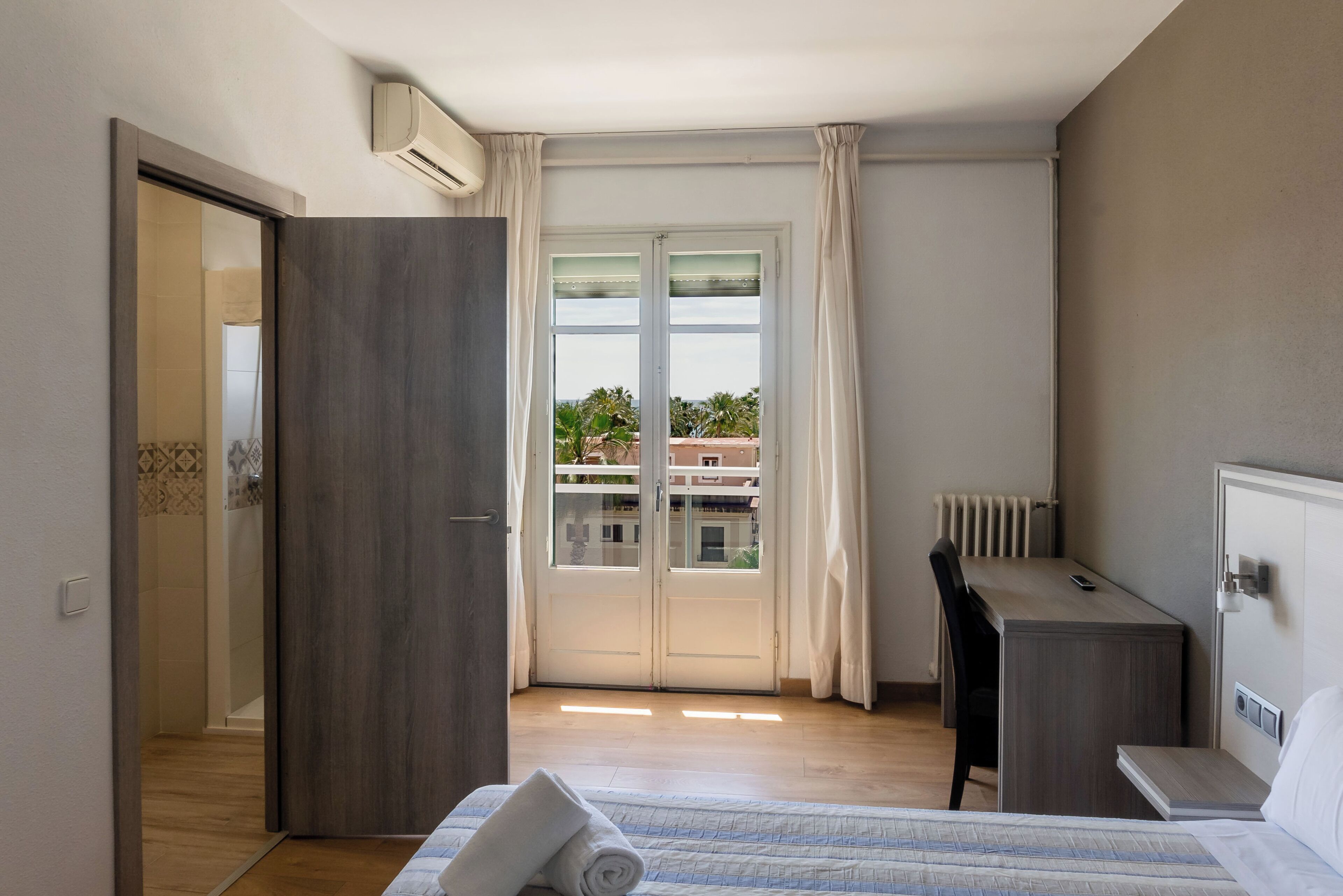 Habitación de hotel con cama, escritorio, silla, radiador y vistas al exterior.