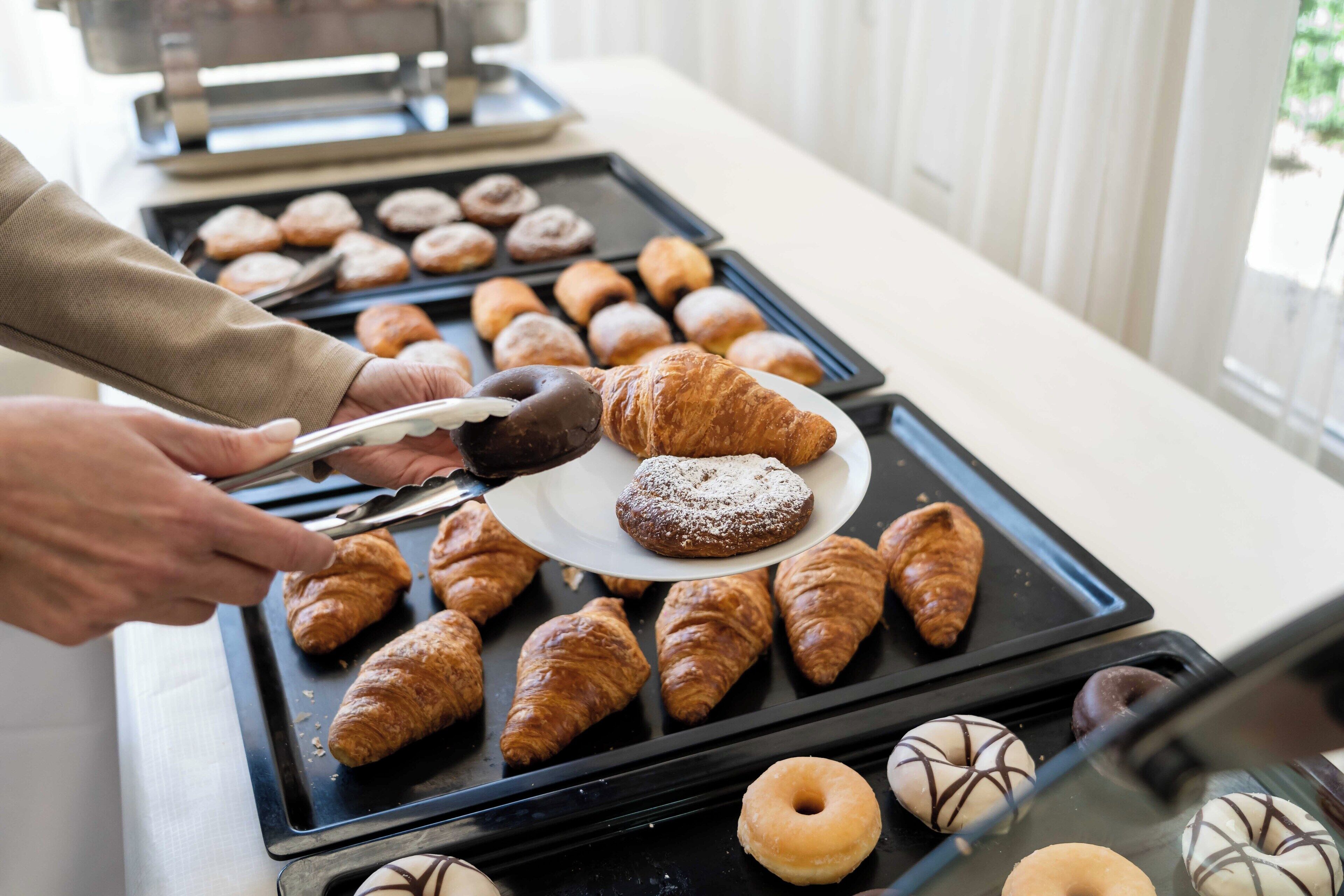 A display of assorted pastries, including croissants and chocolate-covered doughnuts, on trays.