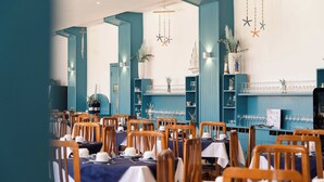 Un restaurante con sillas y mesas de madera, paredes color turquesa y adornos colgantes.