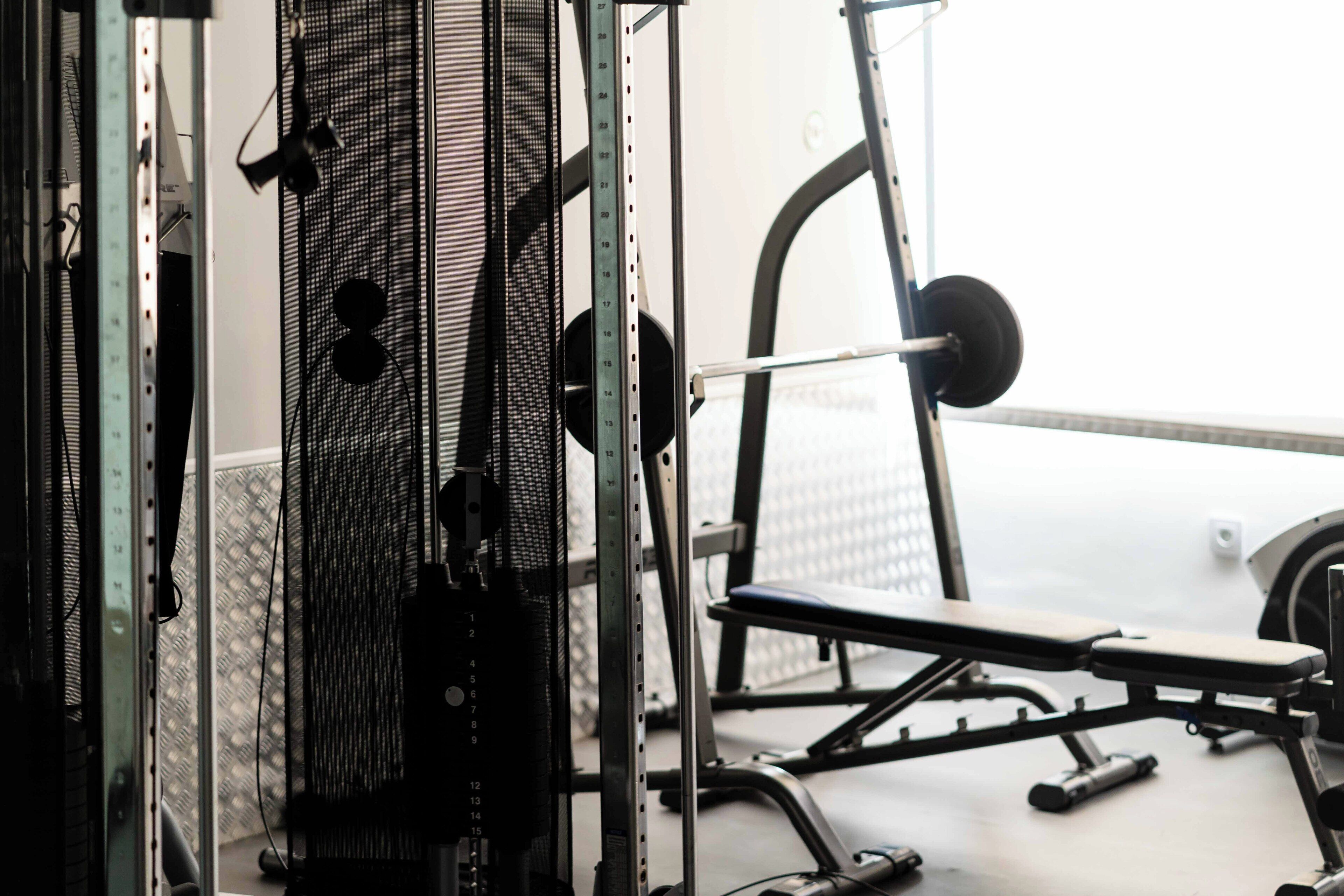 A gym with weightlifting equipment, a bench, and a mirrored wall.