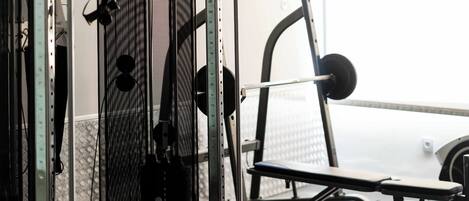 A gym with weightlifting equipment, a bench, and a mirrored wall.